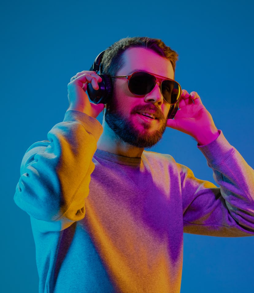 Enjoying his favorite music. Happy young stylish man in hat and sunglasses with headphones listening...