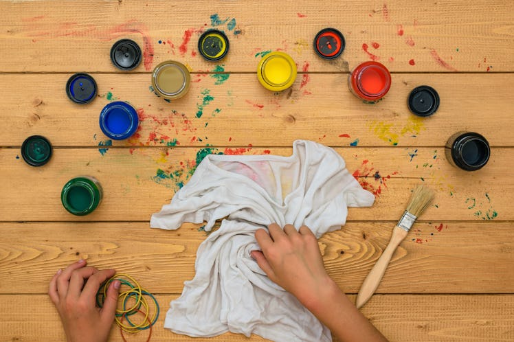 The girl rolls up a white t-shirt for painting in the style of tie dye. Staining fabric in tie dye s...