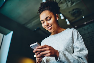 Cheerful african american girl checking mail in social networks using smartphone and wifi connection...