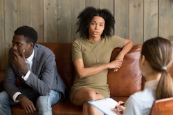 African frustrated wife talking to psychologist sitting on couch with husband, black unhappy woman s...