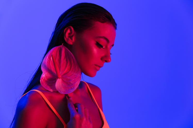 Image of alluring brunette woman wearing bodysuit underwear posing at camera with anthurium plant is...