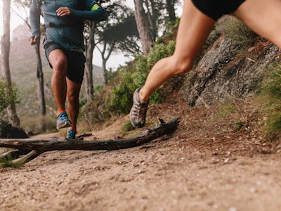 Healthy young couple running on mountain trail in morning. Young man and woman jogging on country pa...