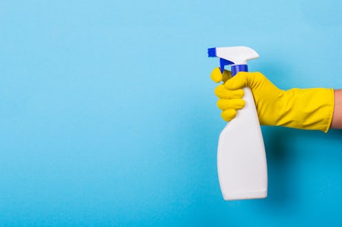 A hand in a yellow glove holds a spray of cleaning fluid on a blue background. Copy space
