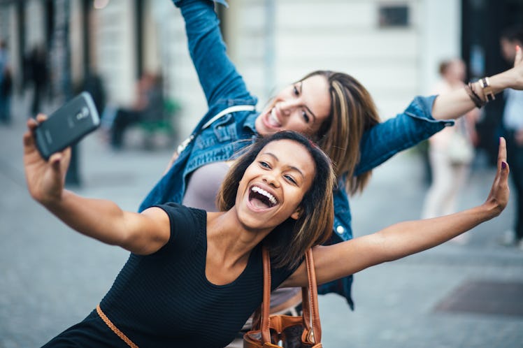 Two women make a silly pose outside while taking a selfie.