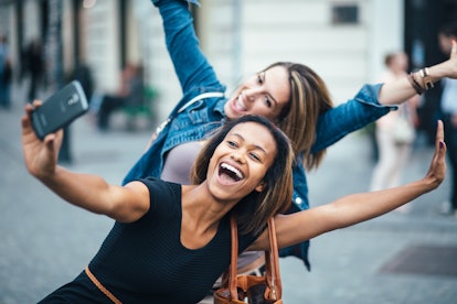 Two women make a silly pose outside while taking a selfie.