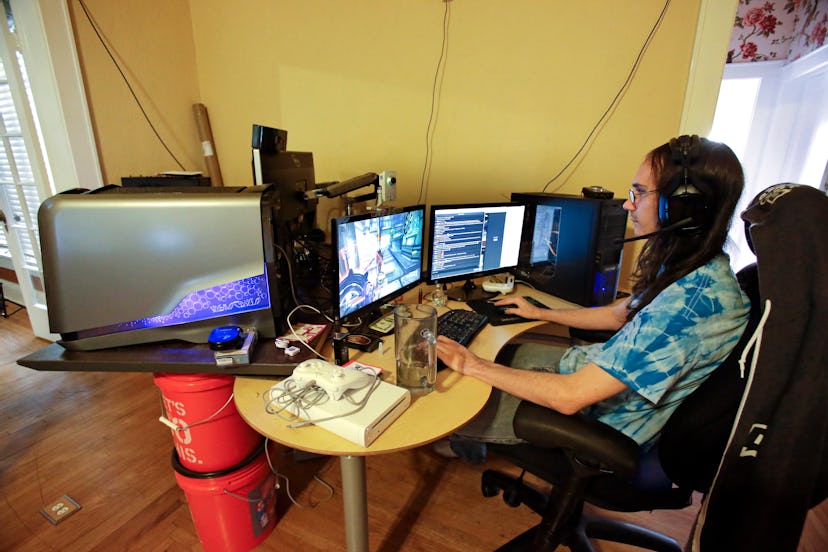 Brett Borden sits at a desk with multiple computers and video screens where he plays video games for...