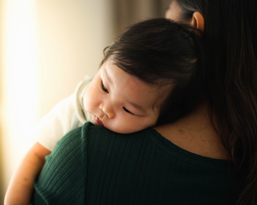 Mother trying to burp her baby by the window