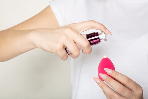 Woman wearing white t shirt applying liquid foundation on a makeup sponge. Closeup shot