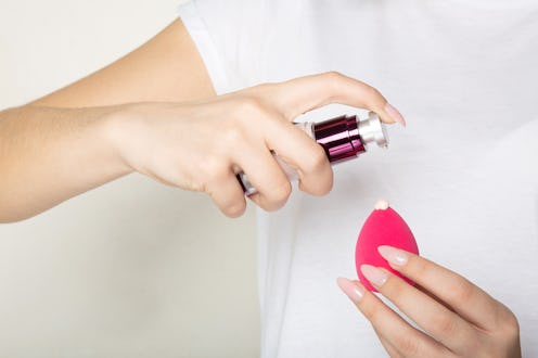 Woman wearing white t shirt applying liquid foundation on a makeup sponge. Closeup shot