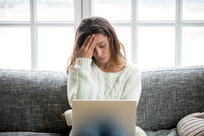 Frustrated sad woman feeling tired worried about problem sitting on sofa with laptop, stressed depre...