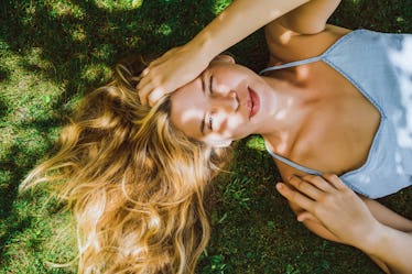 Beautiful girl with long white hair lies on green grass and smiles. Squint. A narrowed eye and a sly...