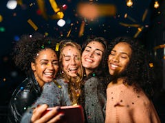 A group of friends all smile for a selfie picture as colorful confetti falls all around them. 