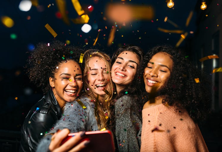 A group of friends all smile for a selfie picture as colorful confetti falls all around them. 