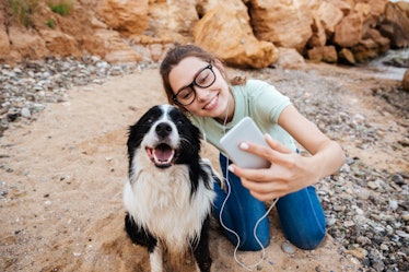 A woman wearing glasses takes a selfie with her dog while they're outside on a walk.