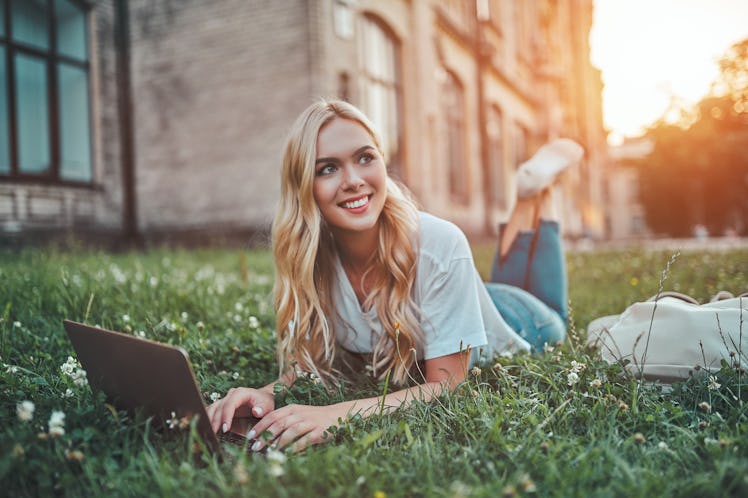 Attractive young woman is studying near university. Female student is lying on grass outdoors with l...