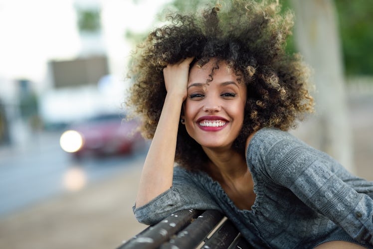 Young mixed woman with afro hairstyle smiling in urban background. Black girl wearing casual clothes...