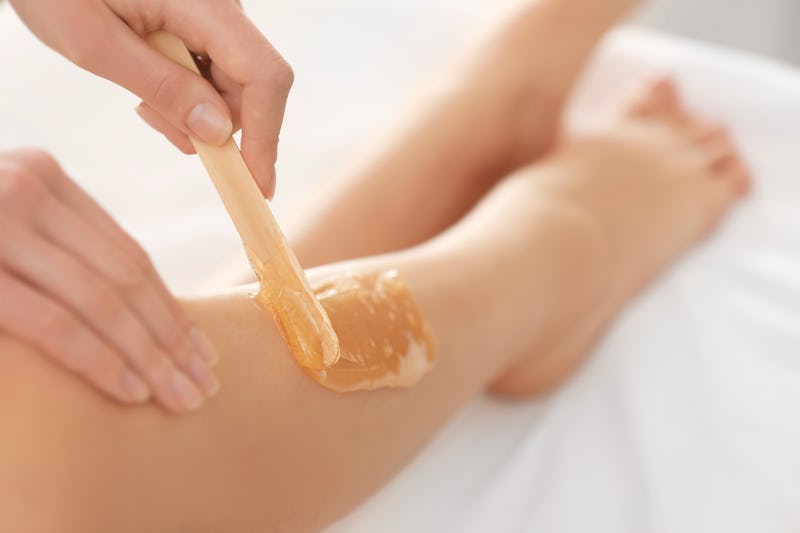 Beautician waxing female legs in spa center