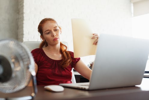 Portrait of young redhead woman working with computer laptop in office at summer during heatwave. Th...