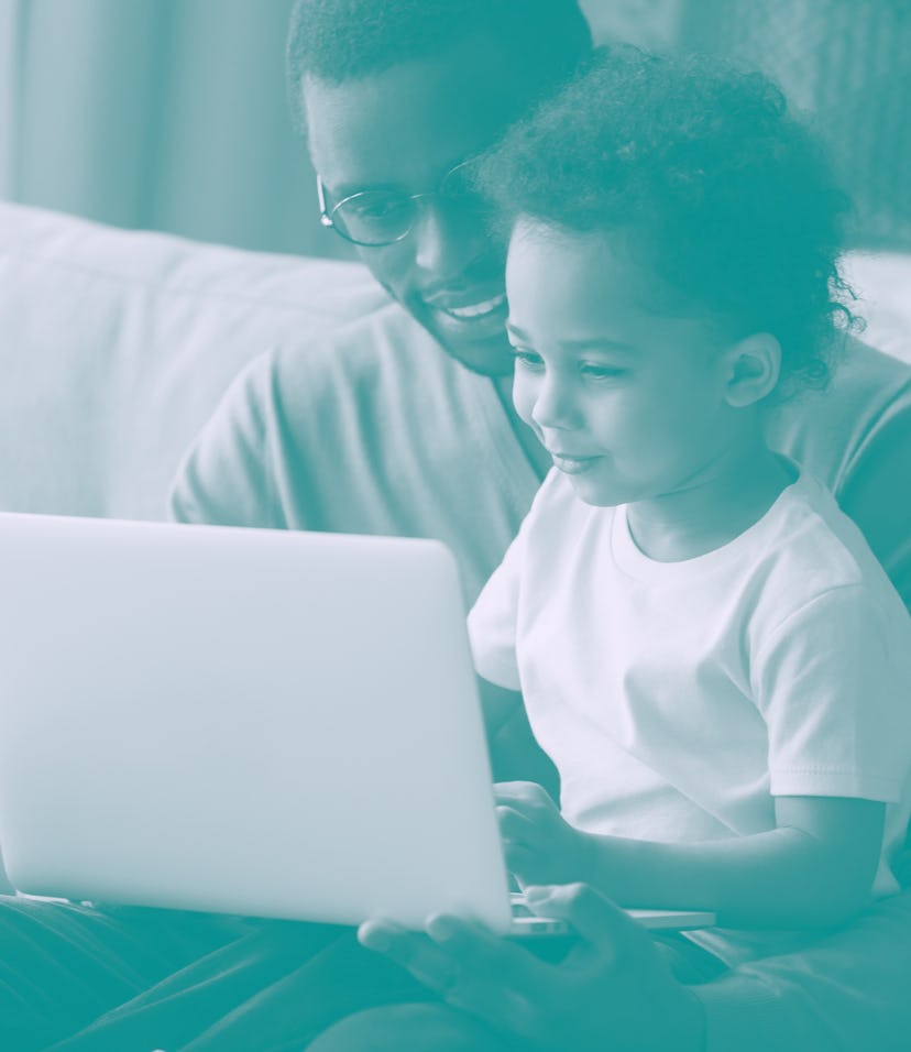 African father holds little son on lap family sitting on sofa at home with notebook, looking at scre...