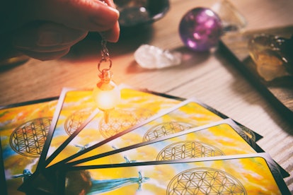 Tarot cards dowsing tool in hand and crystals as a concept of psychic advisor or ways of divination