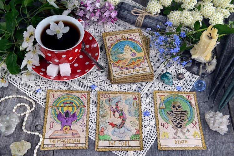 Tarot cards with cup of tea, flowers and black candles on planks. Occult, esoteric and divination st...