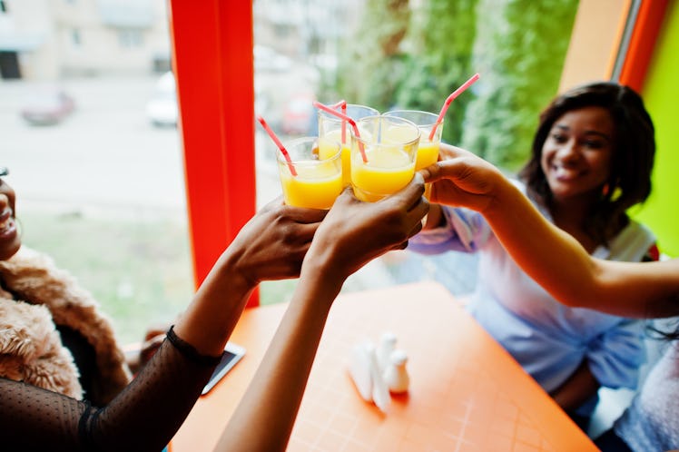 A group of friends cheers their orange juice glasses with pink straws at a table.