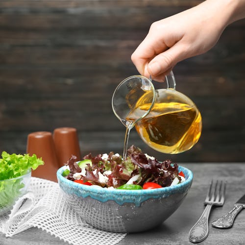 Woman adding tasty apple vinegar to salad with vegetables on table