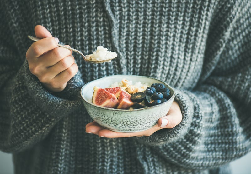 Healthy winter breakfast. Woman in woolen sweater eating rice coconut porridge with figs, berries, h...