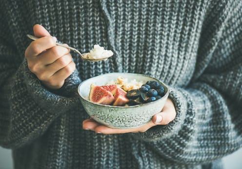Healthy winter breakfast. Woman in woolen sweater eating rice coconut porridge with figs, berries, h...