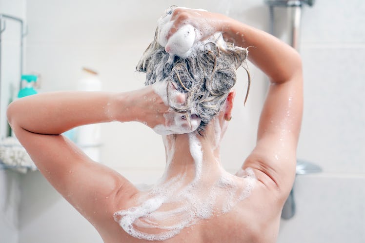 Woman washes her hair with shampoo in bathroom. Woman washing her hair with a lot of foam inside a s...