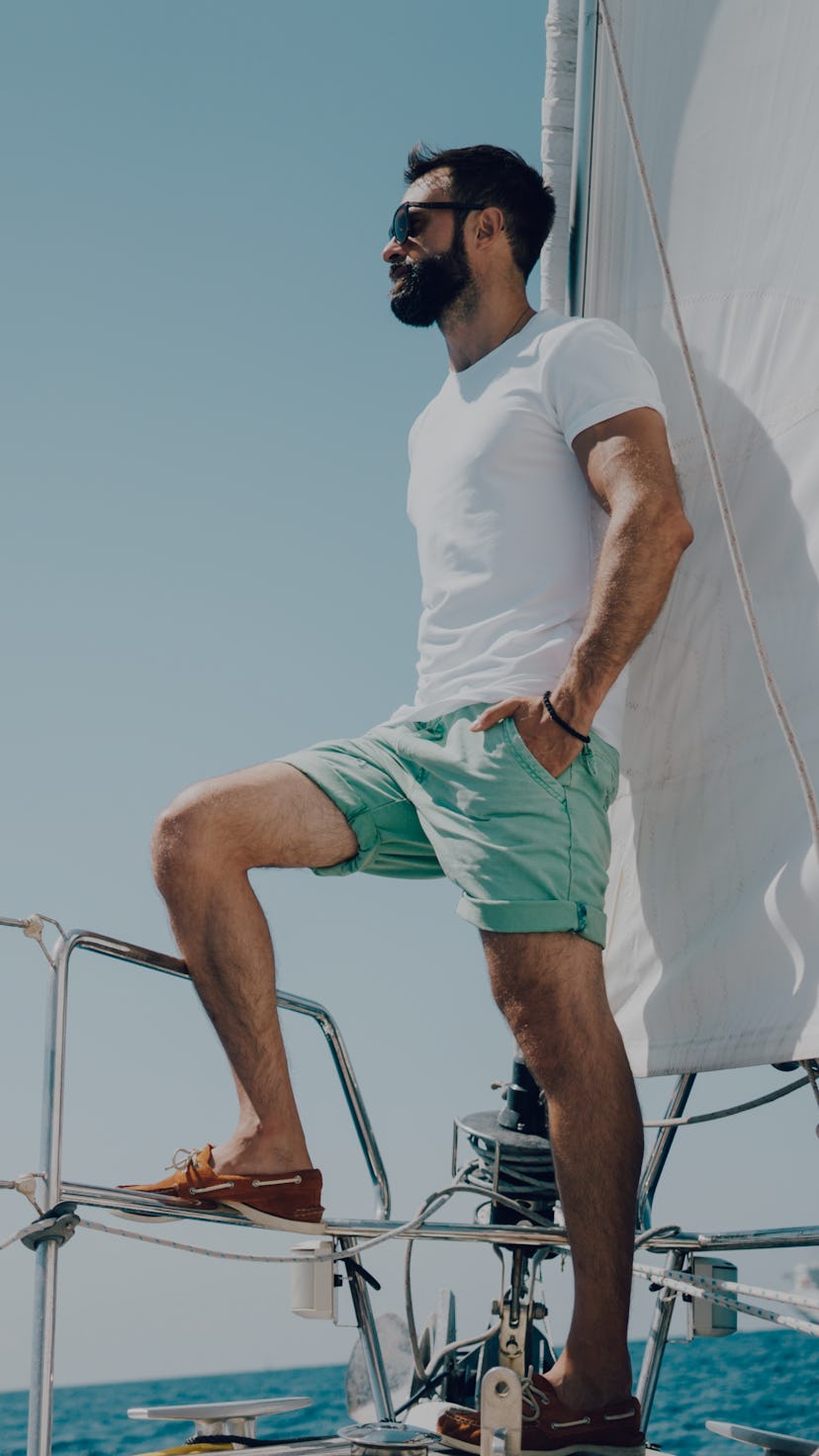 Low angle view of young bearded man standing on the nose yacht