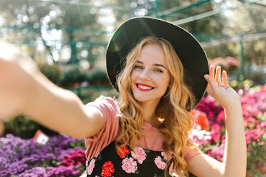 Stunning woman with beautiful eyes making selfie in orangery. Pleased girl in black hat posing with ...