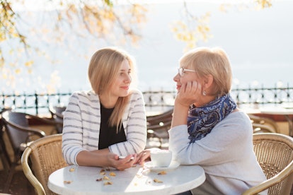 A mother and daughter look at each other and smile while sitting at an outdoor café.