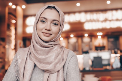 beautiful Muslim girl in hijab smiling, waiting for her food in a restaurant