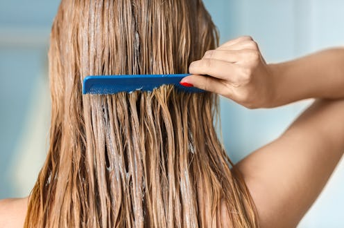 Young woman combing hair covered with mask, indoors