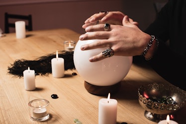 cropped view of psychic holding hands above magical crystal ball near candles 