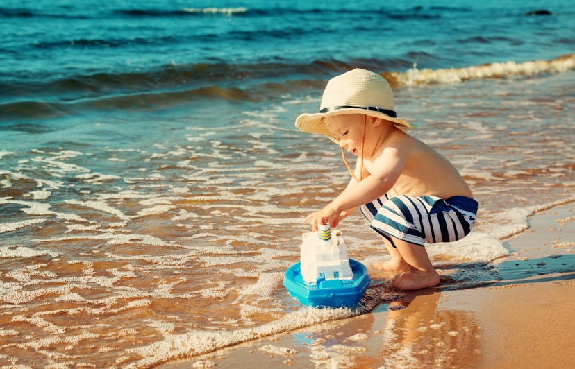 toddler boy playing with toy boat on the beach