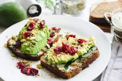 A plate of colorful avocado toast with cranberries on top sits on the table. 
