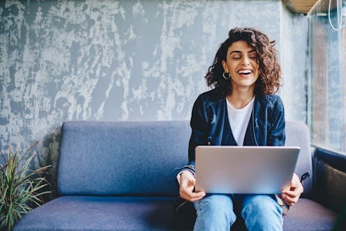 A happy woman sits on her couch at home with her laptop computer.