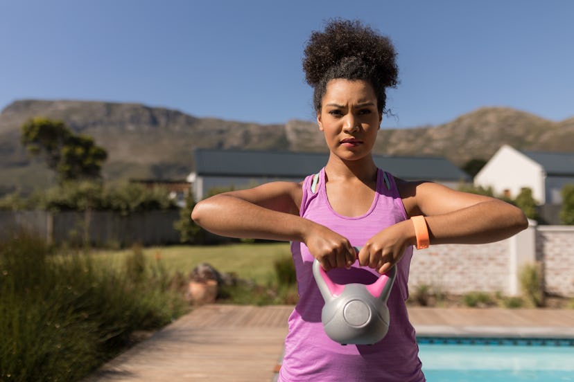Front view of a young African American woman exercising with kettlebell in front of the swimming poo...