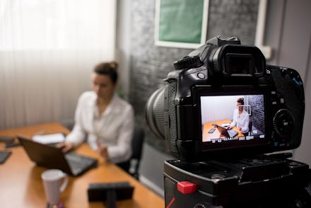 Video camera shoots a young businesswoman sitting at a table in front of a laptop 
