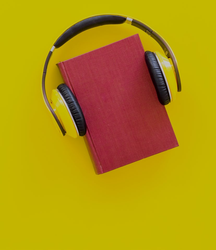 Audiobooks concept. Headphones put over hardback book with empty cover on yellow background top view...