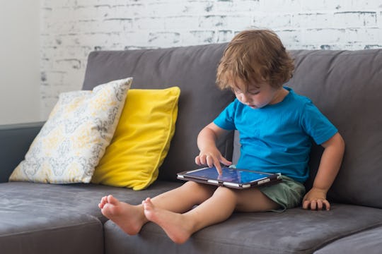 Little cute boy in a blue T-shirt playing games on a tablet and watching cartoons