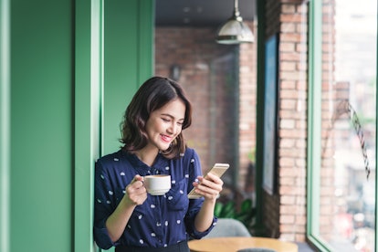 Beautiful cute asian young businesswoman in the cafe, using mobile phone and drinking coffee smiling