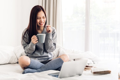 Young woman relaxing and drinking cup of hot coffee or tea using laptop computer on a cold winter da...