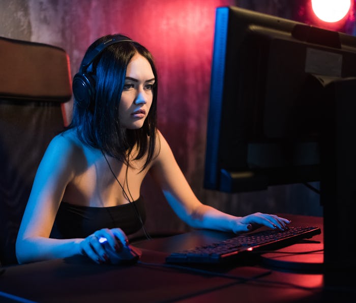 A cute female gamer girl sits in a cozy room behind a computer and plays games. Woman live streaming...