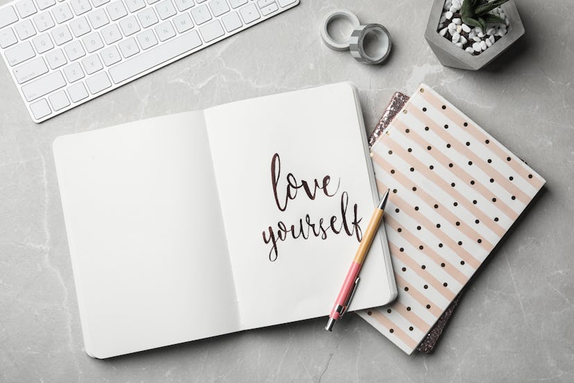 Flat lay composition with words LOVE YOURSELF written in notebook on grey table