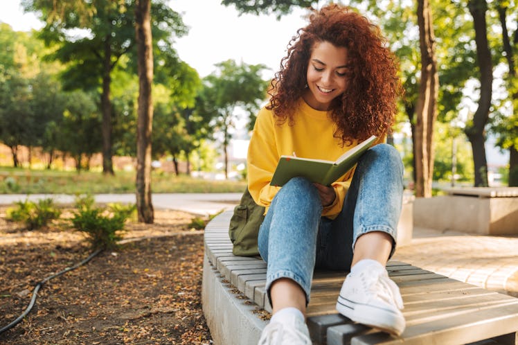 Young woman writes in journal during autumn, having the best week of October 25, 2021, per her zodia...