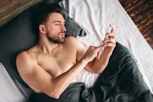 Cheerful young man speaking by cellphone in bedroom. Handsome sporty young guy in underwear is lying...