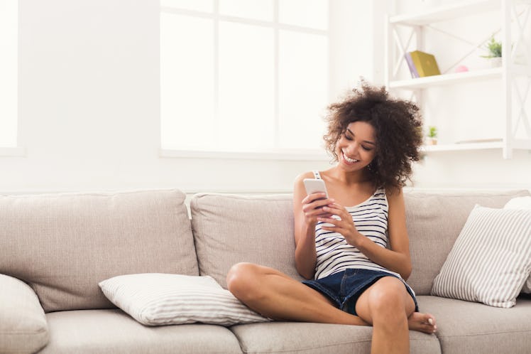 Social networks. Young black woman messaging on smartphone at home, sitting comfortably on beige sof...
